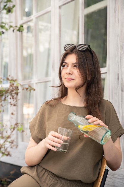 La giovane donna attraente beve l'acqua con il limone