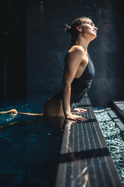 La giovane donna attraente in un costume da bagno nero si sta rilassando in piscina