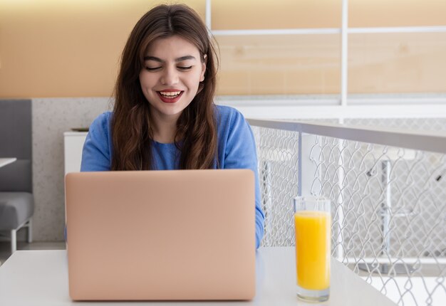 La giovane donna attraente in un maglione blu lavora ad un computer portatile in un caffè.