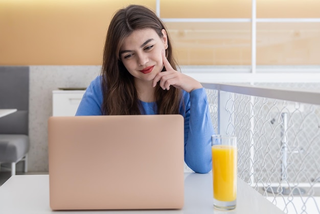 La giovane donna attraente in un maglione blu lavora al computer portatile in un caffè