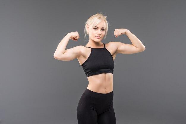 La giovane donna bionda adatta della ragazza sportiva in abiti sportivi neri dimostra il suo forte allungamento del corpo muscoloso