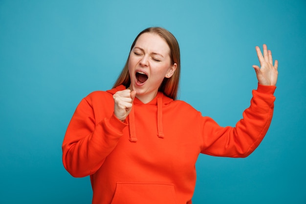 La giovane donna bionda finge che tiene il microfono che solleva la mano che canta con gli occhi chiusi