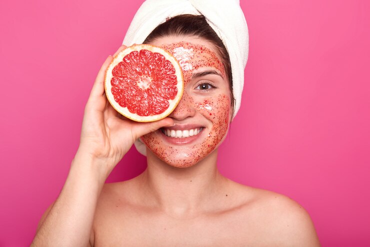 Foto gratuito la giovane donna carismatica emotiva con un bel sorriso sul viso passa il tempo a fare trattamenti di bellezza, rende la pelle fresca e pulita, tiene metà del pompelmo con un asciugamano bianco in testa.