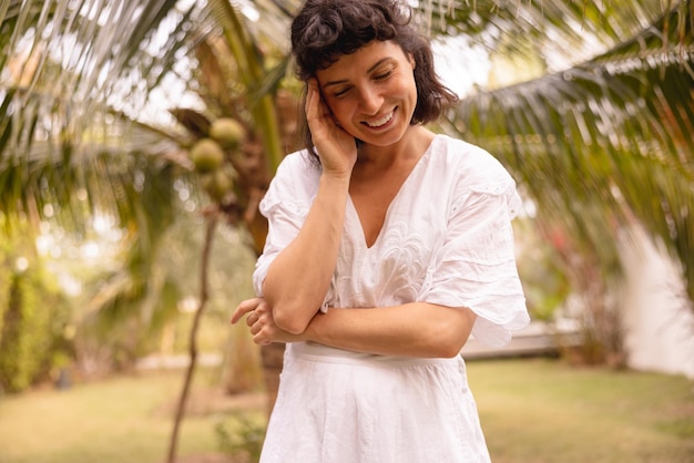 La giovane donna castana caucasica modesta indossa un prendisole bianco con gli occhi chiusi e le braccia incrociate all'aperto in estate