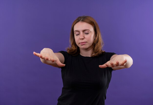 La giovane donna casuale che allunga distribuisce con gli occhi chiusi sulla parete viola isolata