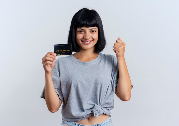 La giovane donna caucasica castana sorridente tiene la carta di credito e tiene il pugno
