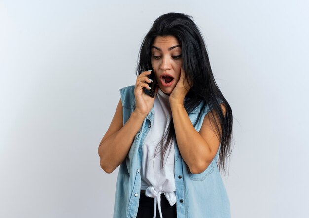 La giovane donna caucasica scioccata mette la mano sul viso parlando al telefono