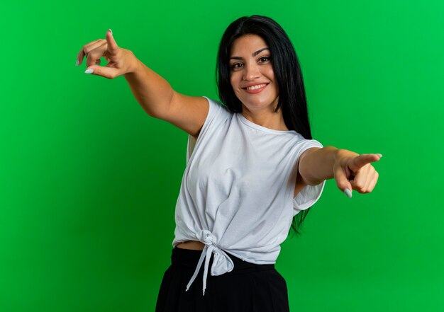 La giovane donna caucasica sorridente indica la macchina fotografica con due mani