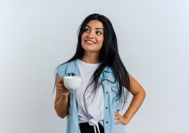 La giovane donna caucasica sorridente tiene la tazza guardando di lato