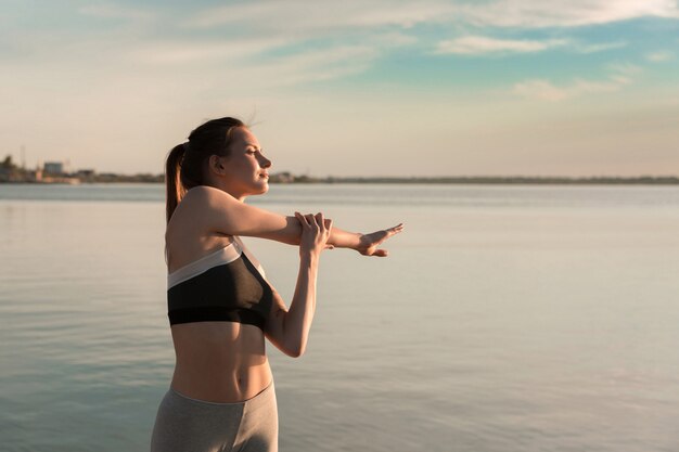 La giovane donna di sport alla spiaggia fa gli esercizi di allungamento.