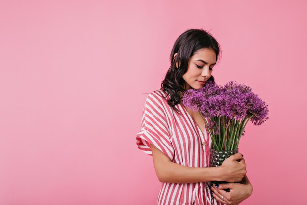 La giovane donna dolce di umore romantico è carina guardando una bracciata di fiori. Ritratto di signora europea in abito elegante.