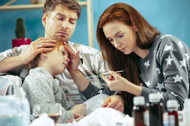 La giovane donna e l'uomo con la figlia ammalata a casa. Trattamento domiciliare. Combattere con una malattia. Assistenza sanitaria. Insufficienza familiare. L'inverno, l'influenza, la salute, il dolore, la paternità, il concetto di relazione