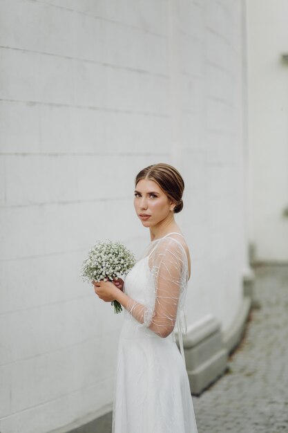 La giovane donna elegante in vestito bianco alla moda sta vicino alla parete