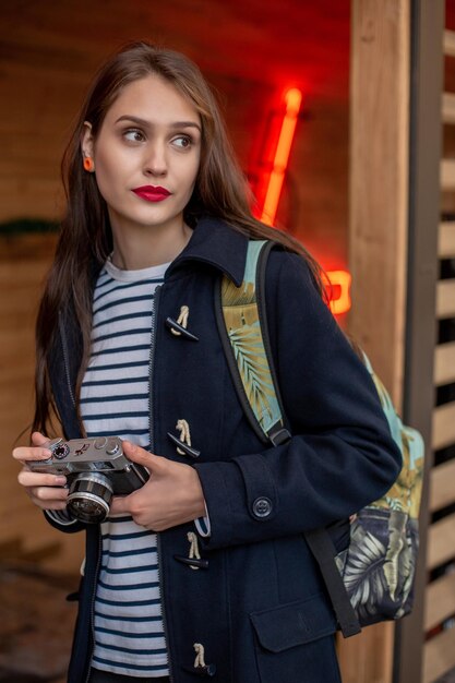 La giovane donna felice dei pantaloni a vita bassa tiene la macchina fotografica retrò. Divertirsi in città con la macchina fotografica, foto di viaggio del fotografo.