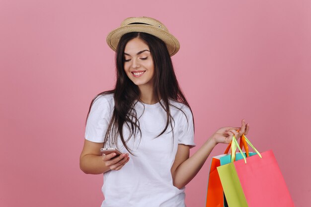 La giovane donna felice utilizza il suo telefono che posa con i sacchetti della spesa variopinti nello studio