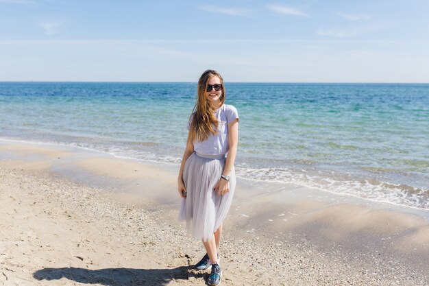 La giovane donna graziosa con i capelli lunghi rimane vicino al mare blu