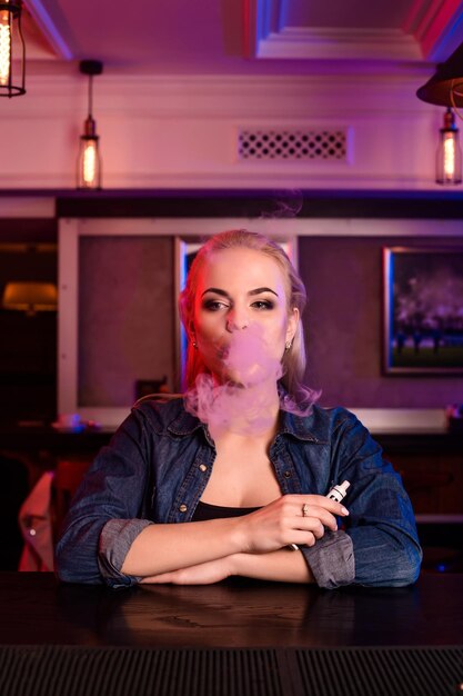 La giovane donna graziosa fuma una sigaretta elettronica al bar di vape. Negozio di vaporizzatori.