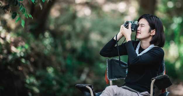 La giovane donna graziosa usa la fotocamera digitale per scattare una foto bella natura mentre si accampa nella foresta con lo spazio della copia di felicità