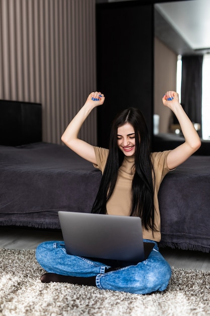 La giovane donna ha finito i suoi compiti sul pavimento usando un laptop con un gesto di vittoria felice e tenendo le mani in alto