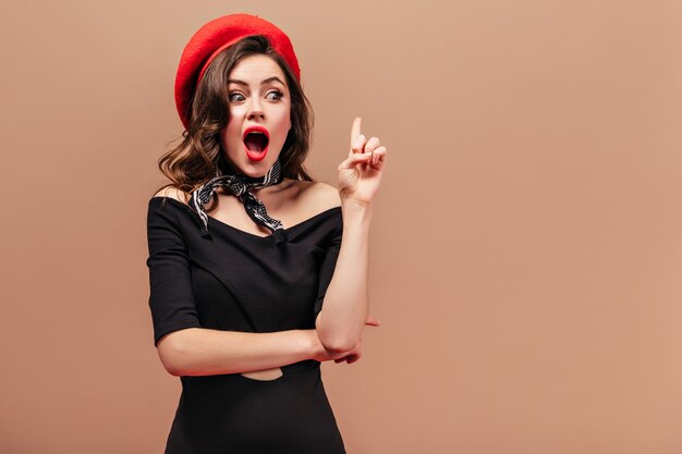 La giovane donna in abito nero, cappello rosso e sciarpa ha pensato a una nuova idea e si è presentata con il dito indice rivolto verso l'alto.