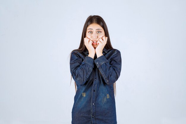 La giovane donna in camicia di jeans sembra spaventata e spaventata