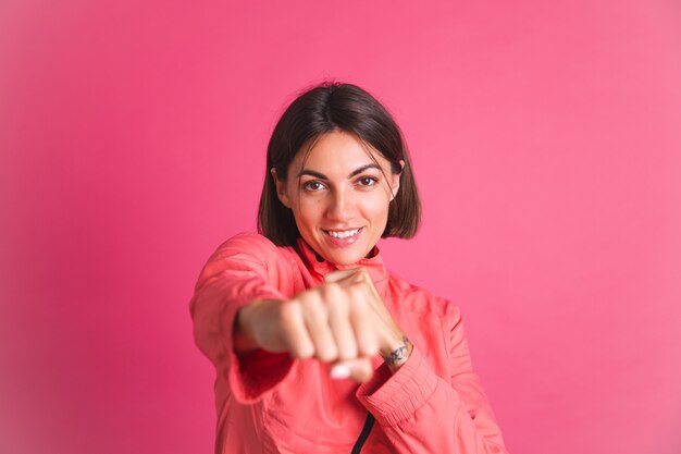 La giovane donna in forma in giacca sportiva sul rosa combatte il gesto della scatola box