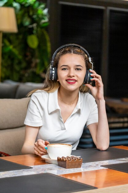 La giovane donna indossa le cuffie e guarda la telecamera al ristorante