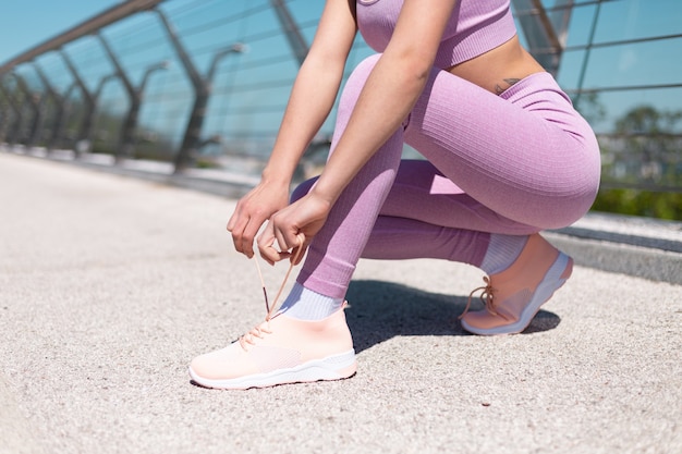 La giovane donna nell'abbigliamento sportivo adatto sul ponte al mattino soleggiato caldo lega i lacci delle scarpe