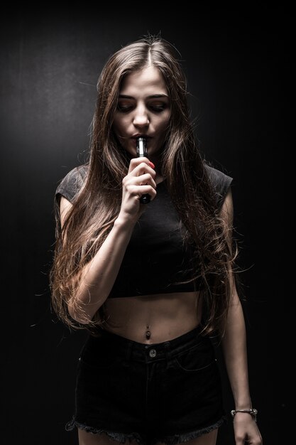 La giovane donna sexy sta fumando la sigaretta elettronica. nuvola di vapore sul muro nero