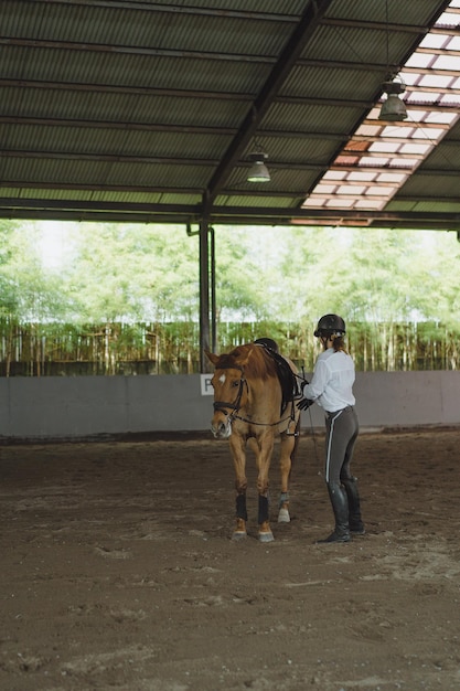 La giovane donna si allena a cavallo nell'arena. Giovane donna caucasica in abbigliamento formale a cavallo attraverso l'arena sabbiosa. Un cavallo di razza per lo sport equestre. La sportiva a cavallo