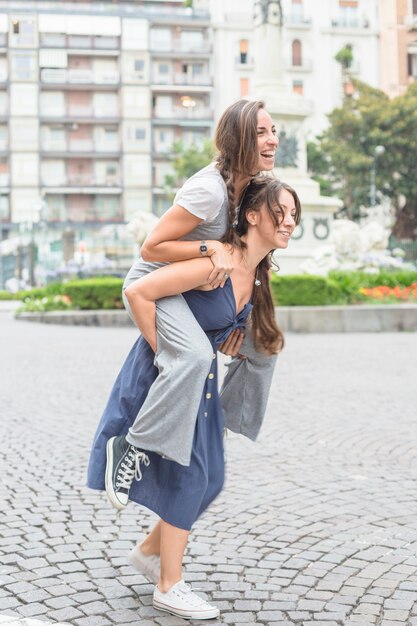 La giovane donna sorridente che prende la sua ragazza sulle spalle guida sulla via