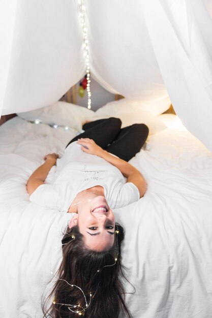 La giovane donna sorridente che si rilassa il letto con il traghetto si accende sui suoi capelli