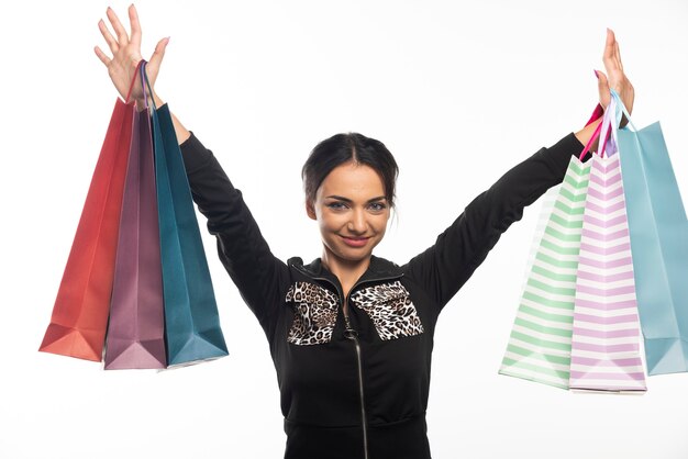 La giovane donna sorridente del ritratto di moda sta mostrando le borse della spesa sul muro bianco