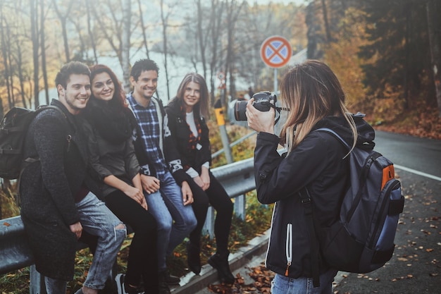 La giovane donna sta scattando una foto dei suoi amici sulla fotocamera digitale nella foresta d'autunno.