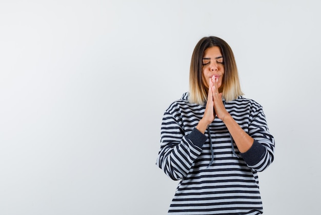 La giovane donna sta sognando tenendo le mani insieme su sfondo bianco