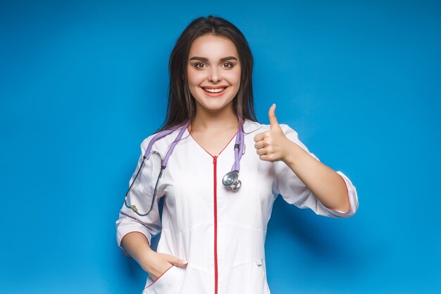 La giovane dottoressa splendida fa okaysign, sull'azzurro. Medicina giovane.