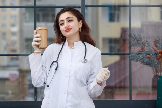 La giovane dottoressa sta in piedi e beve caffè Foto di alta qualità