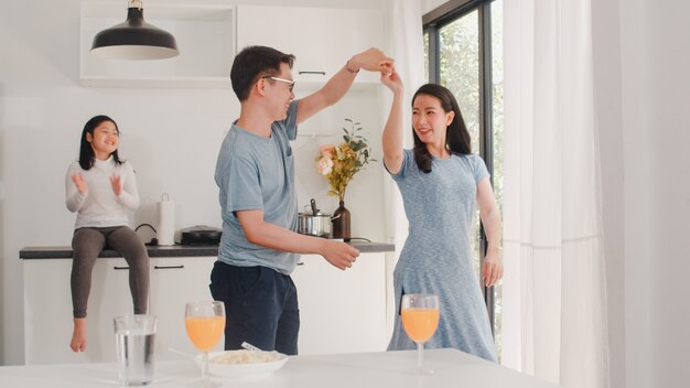 La giovane famiglia asiatica felice ascolta musica e balla dopo la colazione a casa. Attraente madre giapponese padre e figlia stanno godendo trascorrere del tempo insieme in cucina moderna al mattino.