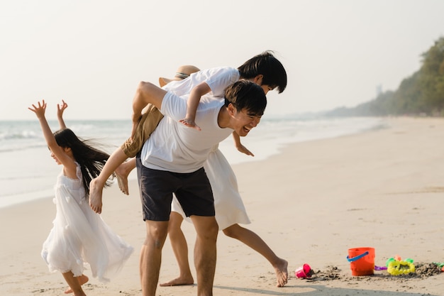 La giovane famiglia felice asiatica gode della vacanza sulla spiaggia la sera. Papà, mamma e bambino si rilassano giocando insieme vicino al mare quando il tramonto durante le vacanze di viaggio. Stile di vita di viaggio vacanze vacanze estate concetto.