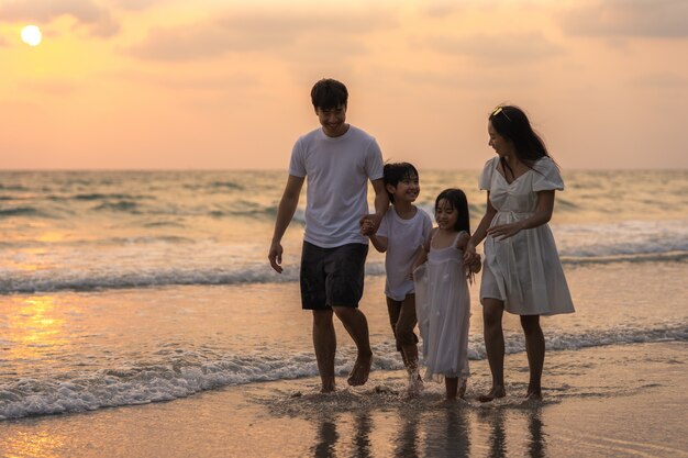 La giovane famiglia felice asiatica gode della vacanza sulla spiaggia nella sera. Papà, mamma e bambino si rilassano camminando insieme vicino al mare quando il tramonto durante un viaggio di vacanza. Stile di vita di viaggio vacanze vacanze estate concetto.