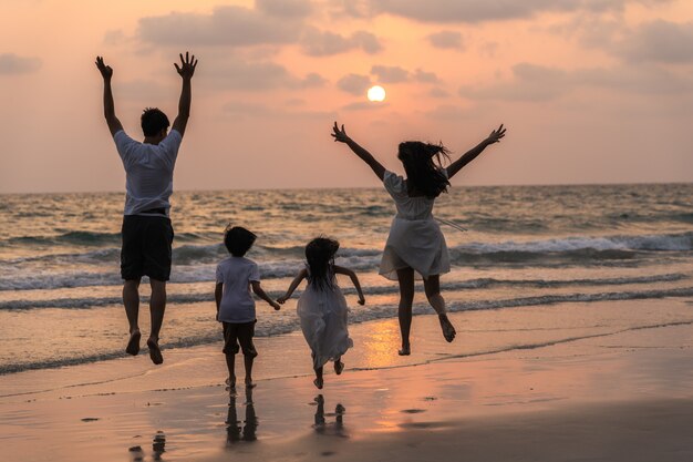 La giovane famiglia felice asiatica gode della vacanza sulla spiaggia nella sera. Papà, mamma e bambino si rilassano correndo insieme vicino al mare mentre silhouette tramonto. Stile di vita di viaggio vacanze vacanze estate concetto.