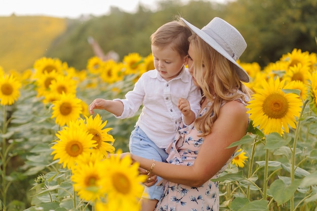 La giovane famiglia felice, il padre e il figlio della madre, stanno sorridendo, tenendo e abbracciando nel giacimento del girasole