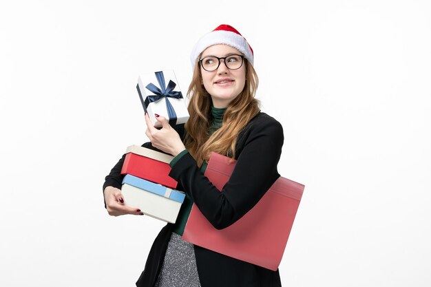 La giovane femmina di vista frontale che tiene i regali di festa sui regali bianchi della parete prenota il nuovo anno
