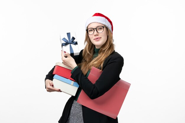 La giovane femmina di vista frontale che tiene i regali di festa sul regalo bianco della parete prenota il nuovo anno