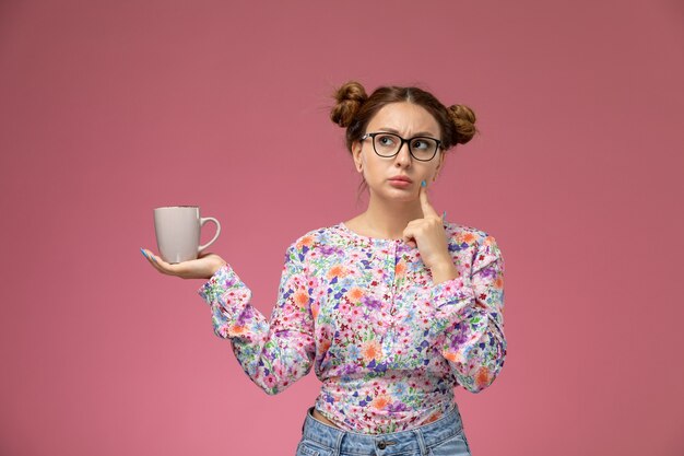 La giovane femmina di vista frontale in fiore ha progettato la camicia e le blue jeans che posano con l'espressione di pensiero sui precedenti chiari