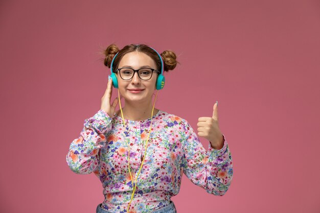 La giovane femmina di vista frontale in fiore ha progettato la camicia e le blue jeans che sorridono ascoltando la musica sui precedenti rosa