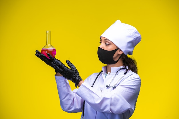 La giovane infermiera nella maschera della mano e del viso tiene la boccetta chimica con entrambe le mani.
