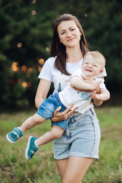 La giovane madre adorabile va a fare una passeggiata con il suo piccolo bambino caucasico nel parco