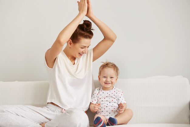 La giovane madre con il suo piccolo figlio di un anno in pigiama sta rilassando e giocando