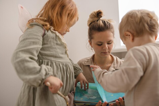 La giovane madre madre gioca con i bambini mostra le immagini nel libro a sua figlia e suo figlio a casa Concetto di persone di stile di vita reale